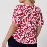 Back view of plus sized model wearing Lila Top in Cherry Charm. A flutter sleeve top with a short tail hem line, made of dry touch jersey fabric that is cooling and comfortable. Womens clothing brand Leina & Fleur  from 8-24 proudly stocks sizes 8-24.