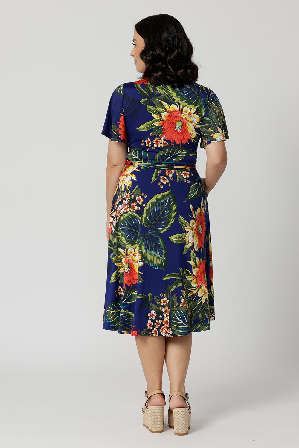 Back view image of petite model wearing floral wrap dress. Easy care summer dress is made of slinky jersey that is crease-resistant perfect for packing in a suitcase. Comfortable fit dress is flattering and relaxed for all occasions. Leina & Fleur stock this wrap dress in sizes 8-24. 