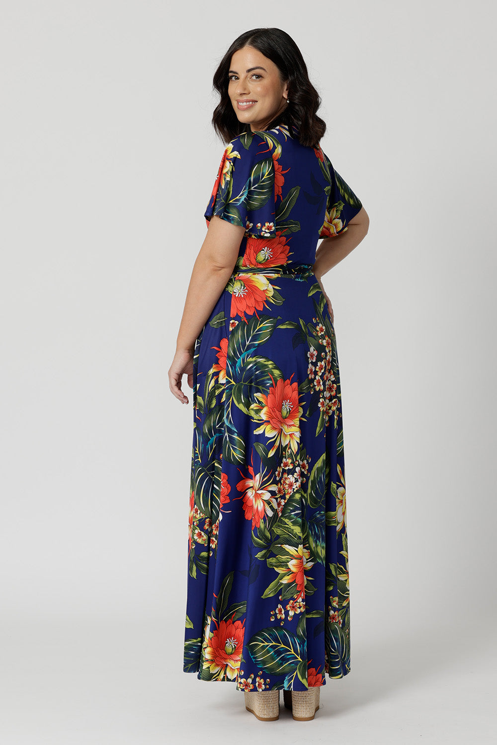 Back view image of petite sized model wearing floral wrap dress. Easy care top is made of slinky jersey that is crease-resistant perfect for travel. Comfortable floral dress is flattering and relaxed for all-day travel wear. Leina & Fleur stock sizes 8-24. 