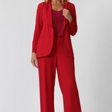 A size 12 woman wears the Merit Blazer in Flame, a textured scuba crepe blazer with button front. This red work blazer is worn with red workwear pants and red cami top. Curved hemline and front pockets. Made in Australia for women size 8 - 24.