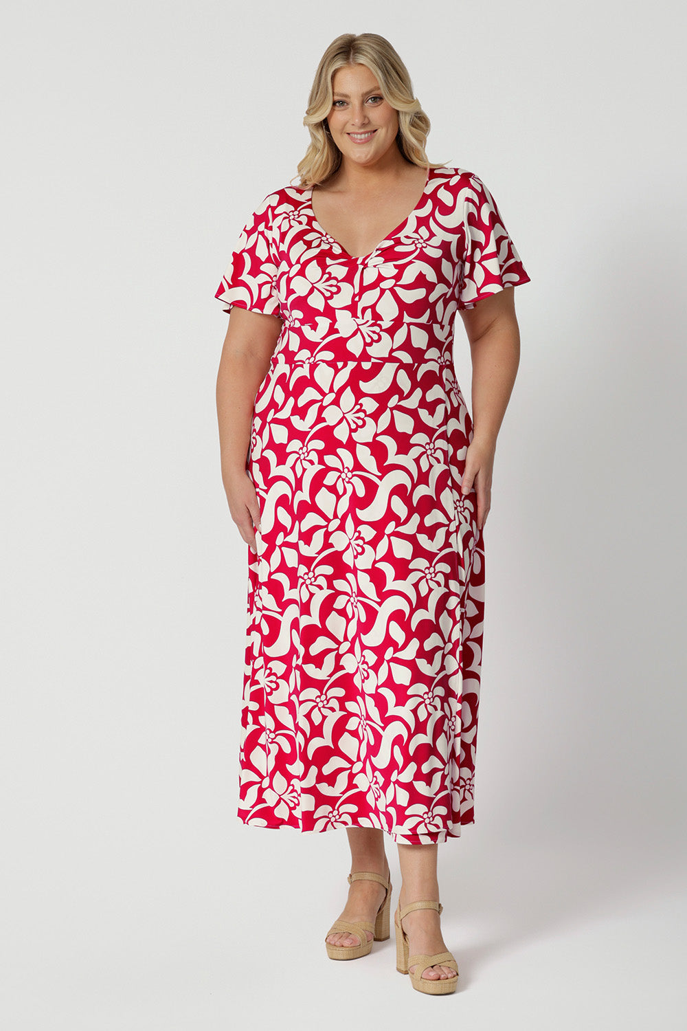 Plus sized woman wears floral printed maxi dress with twist bodice and flutter sleeve detail. This easy-care and crease-resistant dress is perfect for travel. Designed in Australia with easy care fabric made of red jersey with ivory details. Leina & Fleur clothing brand actively stocks sizes from 8-24. Shop this summer ready dress now.