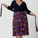 Size 18 curvy woman wears the Nerida dress. Functioning fit and flare wrap dress with a navy bodice and printed skirt. 3/4 Sleeves and functioning pockets. Made in Australia for women. Size 8 - 24. Styled back with a brown sling back heel.