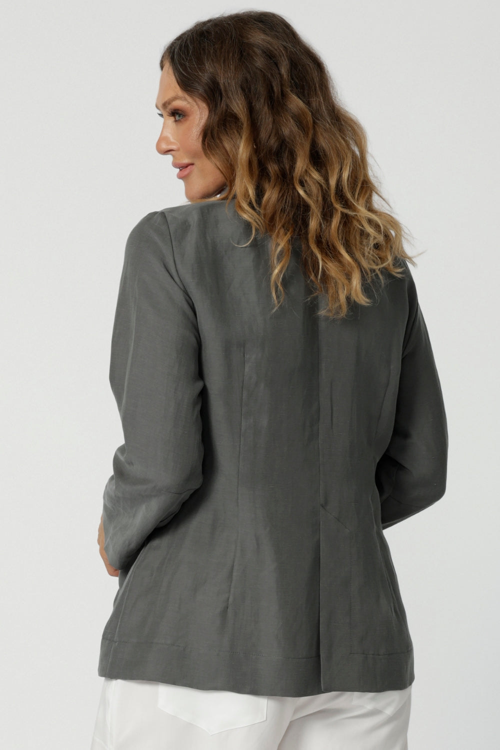 Back view image of 40 year old woman wears cool toned blazer. Light weight and breathable designs helps stay cool  while travelling or during warmer weather. Linen blend blazer is stocked in sizes 8-24 online at Leina & Fleur. 