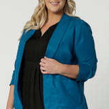 Vibrant teal blazer pictured on plus sized woman is perfect for summer travel. Made with linen, tencel and cupro fabric this blazer is light weight and breathable. Clothing brand Leina & Fluer stock sizes in this travel read blazer in 8-24.