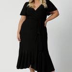 A curvy size 18 woman over 35 is wearing a maxi wrap dress in black for a wedding guest outfit. Made in Australia by Australian fashion brand Leina & Fleur in sizes 8 to 24.