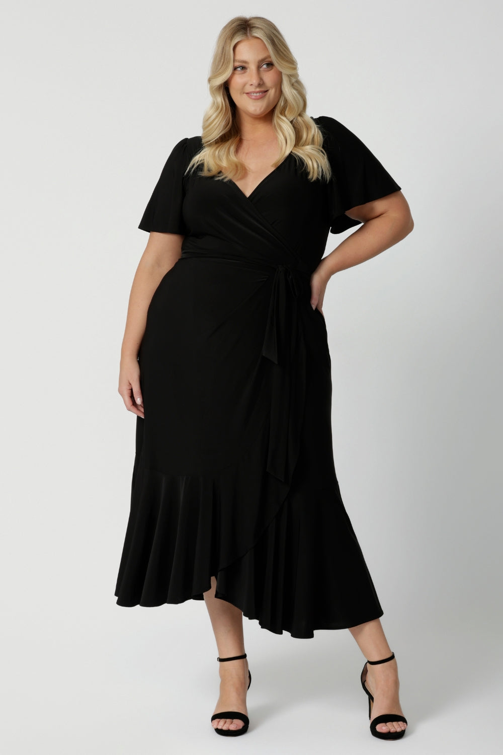 A curvy size 18 woman over 35 is wearing a maxi wrap dress in black for a wedding guest outfit. Made in Australia by Australian fashion brand Leina & Fleur in sizes 8 to 24.