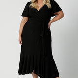 A curvy size 18 woman over 35 is wearing a maxi wrap dress in black for a wedding guest outfit. Made in Australia by Australian fashion brand Leina & Fleur in sizes 8 to 24.