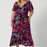 A size 18 woman over 35 wears a maxi wrap dress in a bold print. An elegant wrap dress with a tiered ruffle skirt,  sweetheart neckline and flutter sleeve. Made in Australia for women size 8 - 24 by Leina & Fleur.