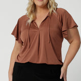 A good summer top for curvy women, a size 18 woman wears a plus size flutter sleeve top in clay slinky jersey fabric. An easy-care top for travel and cruise wear, this made-in-Australia V neck top is worn with tapered leg black travel pants.  By Australian and New Zealand women's clothing brand, Leina and Fleur shop petite to plus size tops for women  online.