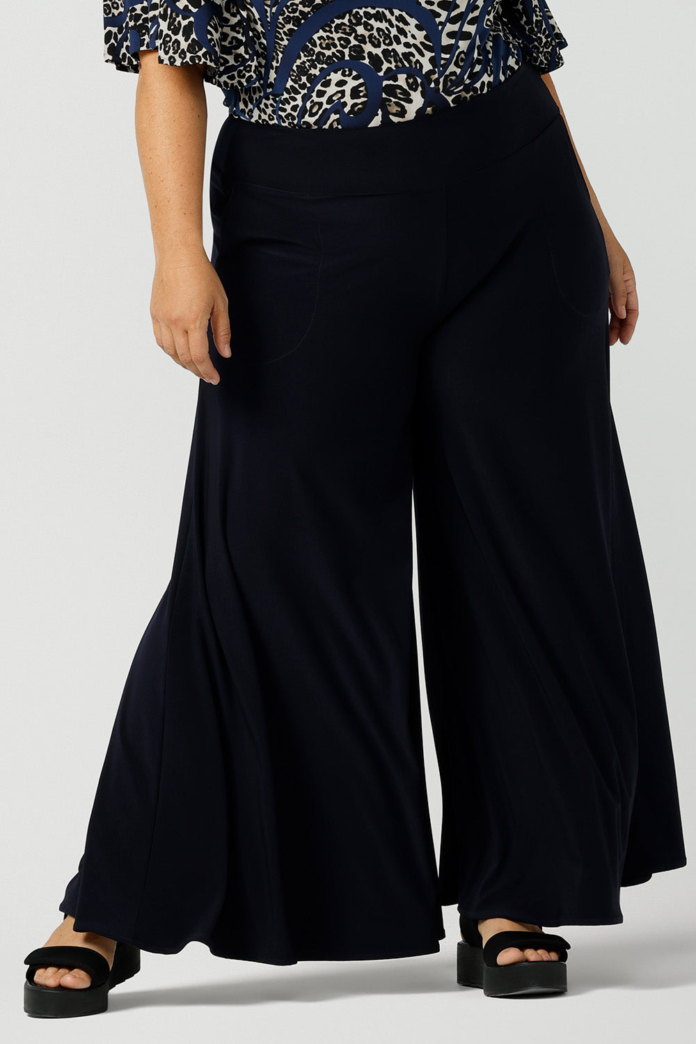 A curvy, size 16 woman wears navy wide leg pants with pockets. These pull-on, easy care pants are comfortable for your everyday capsule wardrobe. Shop these Australian-made wide leg trousers online in sizes 8 to 24, petite to plus sizes.