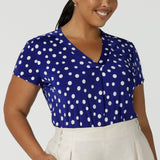 Size 16 Woman wears a cobalt blue spot top with flutter sleeves, high low hemline and v-neck. Soft slinky jersey. Made in Australia for women size 8 to 24.