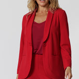 A size 12 woman wears the Merit Blazer in Flame, a textured scuba crepe blazer with button front. This red work blazer is worn with red workwear pants and red cami top. Curved hemline and front pockets. Made in Australia by womens fashion label L&F in sizes 8 - 24.