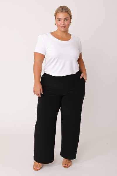 A curvy petite height woman wears black work pants in petite length with a white bamboo jersey T-shirt top. Great pants for short women, these Australian-made pull-on trousers are available in sizes 8 to 24, petite to plus sizes.
