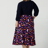 Back view of a size 18 curvy woman wears the Nerida dress. Functioning fit and flare wrap dress with a navy bodice and printed skirt. 3/4 Sleeves and functioning pockets. Made in Australia for women. Size 8 - 24. Styled back with a brown sling back heel.