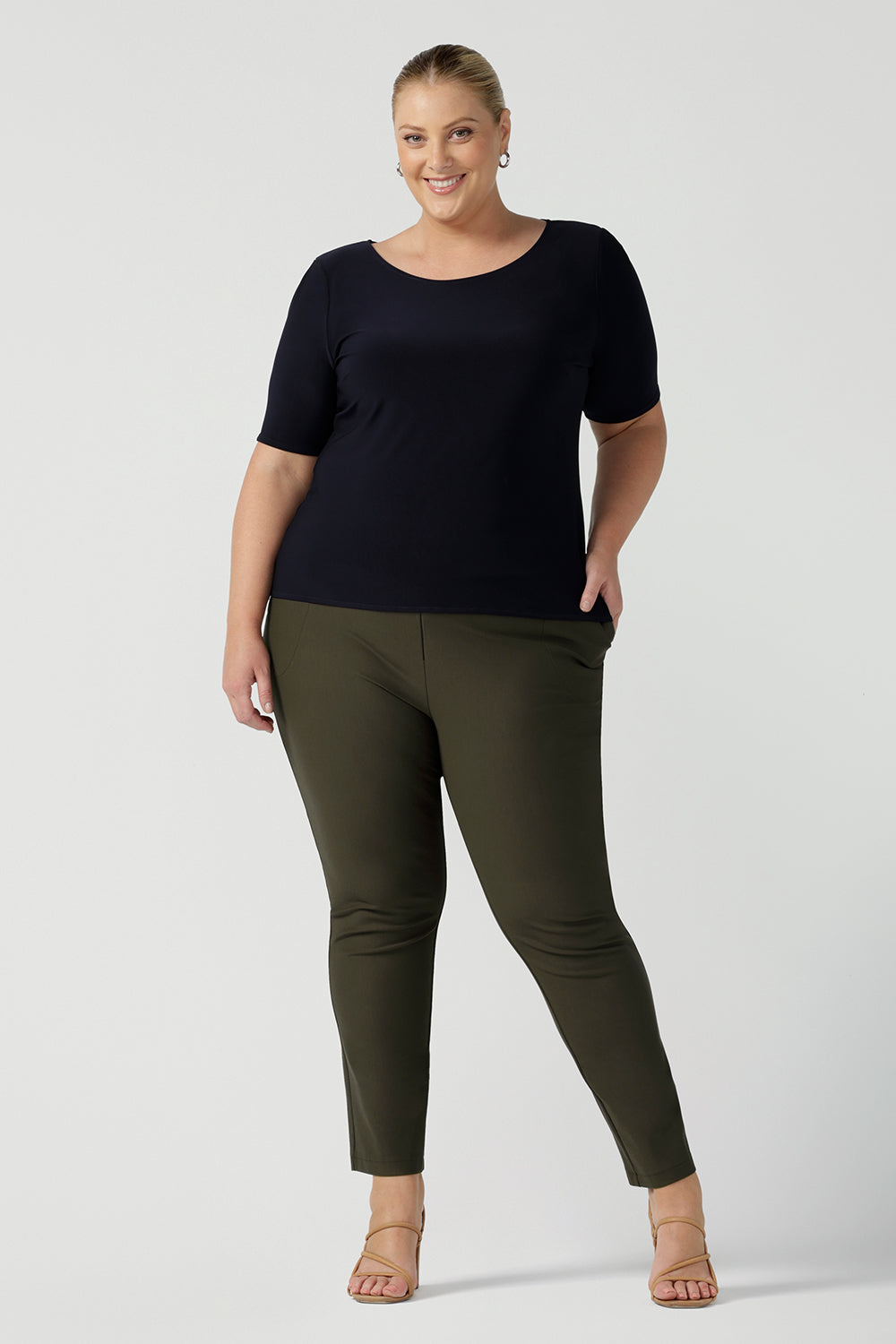 A good top for plus size, curvy women, this short sleeve, boat neck top in navy blue is worn with slim leg tailored pants in olive green ponte fabric. Shown on a size 18 woman, this is a quality top for workwear. Shop slim fit jersey tops made in Australia by women's clothing brand, Leina & Fleur in their online store now!
