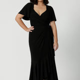 A petite-height woman is wearing a maxi wrap dress in black as a black tie event outfit. Made in Australia by Australian fashion brand Leina & Fleur in sizes 8 to 24.