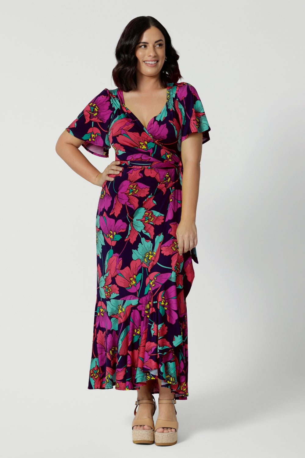 A petite-height woman is wearing a maxi wrap dress in a bold floral print. Made in Australia by Australian fashion brand Leina & Fleur in sizes 8 to 24.