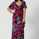 A petite-height woman is wearing a maxi wrap dress in a bold floral print. Made in Australia by Australian fashion brand Leina & Fleur in sizes 8 to 24.