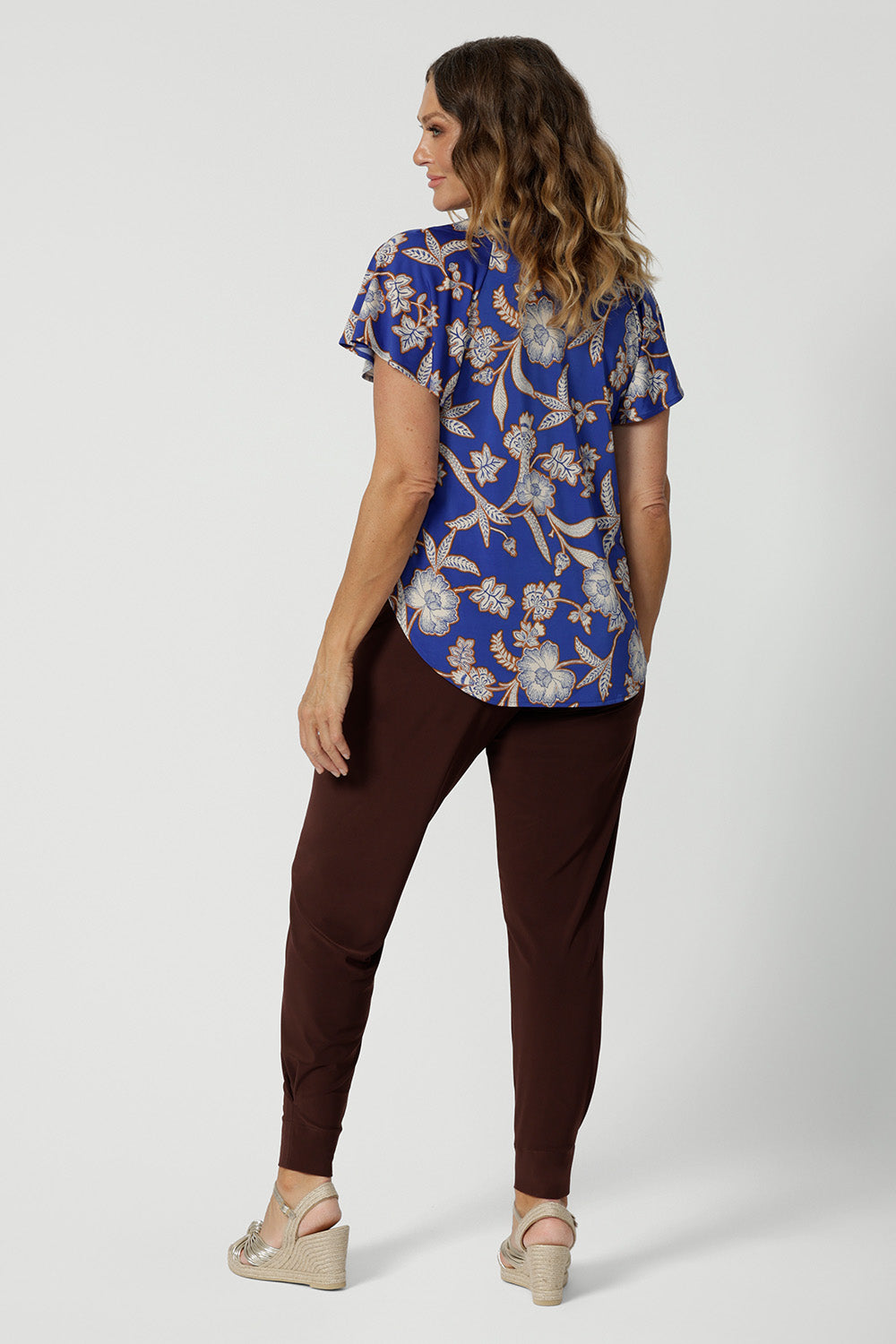 Back view of a good summer top with flutter sleeves for over 50s women, the relaxed fit of this jersey top looks good with espresso brown tapered leg travel pants. With a holiday print and in lightweight, easy care jersey, this is the perfect top for travel and cruise wear. Made in Australia by Australian and New Zealand women's clothing brand Leina & Fleur shop petite to plus size tops online.