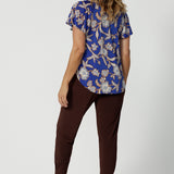 Back view of a good summer top with flutter sleeves for over 50s women, the relaxed fit of this jersey top looks good with espresso brown tapered leg travel pants. With a holiday print and in lightweight, easy care jersey, this is the perfect top for travel and cruise wear. Made in Australia by Australian and New Zealand women's clothing brand Leina & Fleur shop petite to plus size tops online.