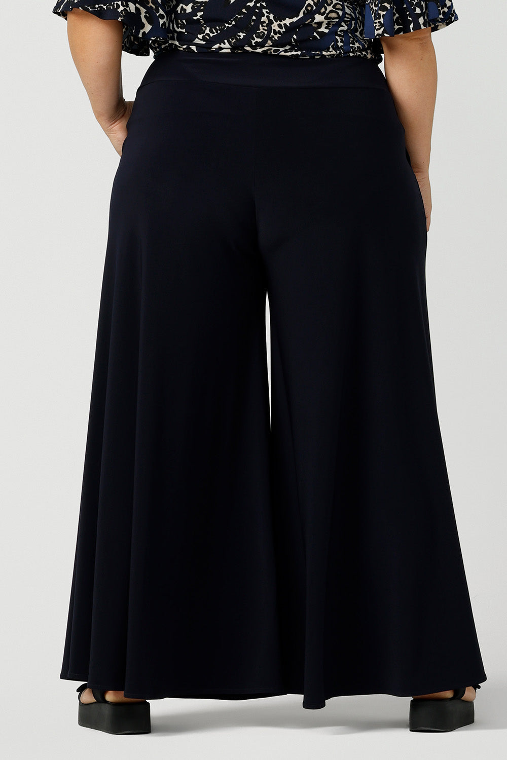 Back view of A curvy, size 16 woman wears navy wide leg pants with pockets. These pull-on, easy care pants are comfortable for your everyday capsule wardrobe. Shop these Australian-made wide leg trousers online in sizes 8 to 24, petite to plus sizes.