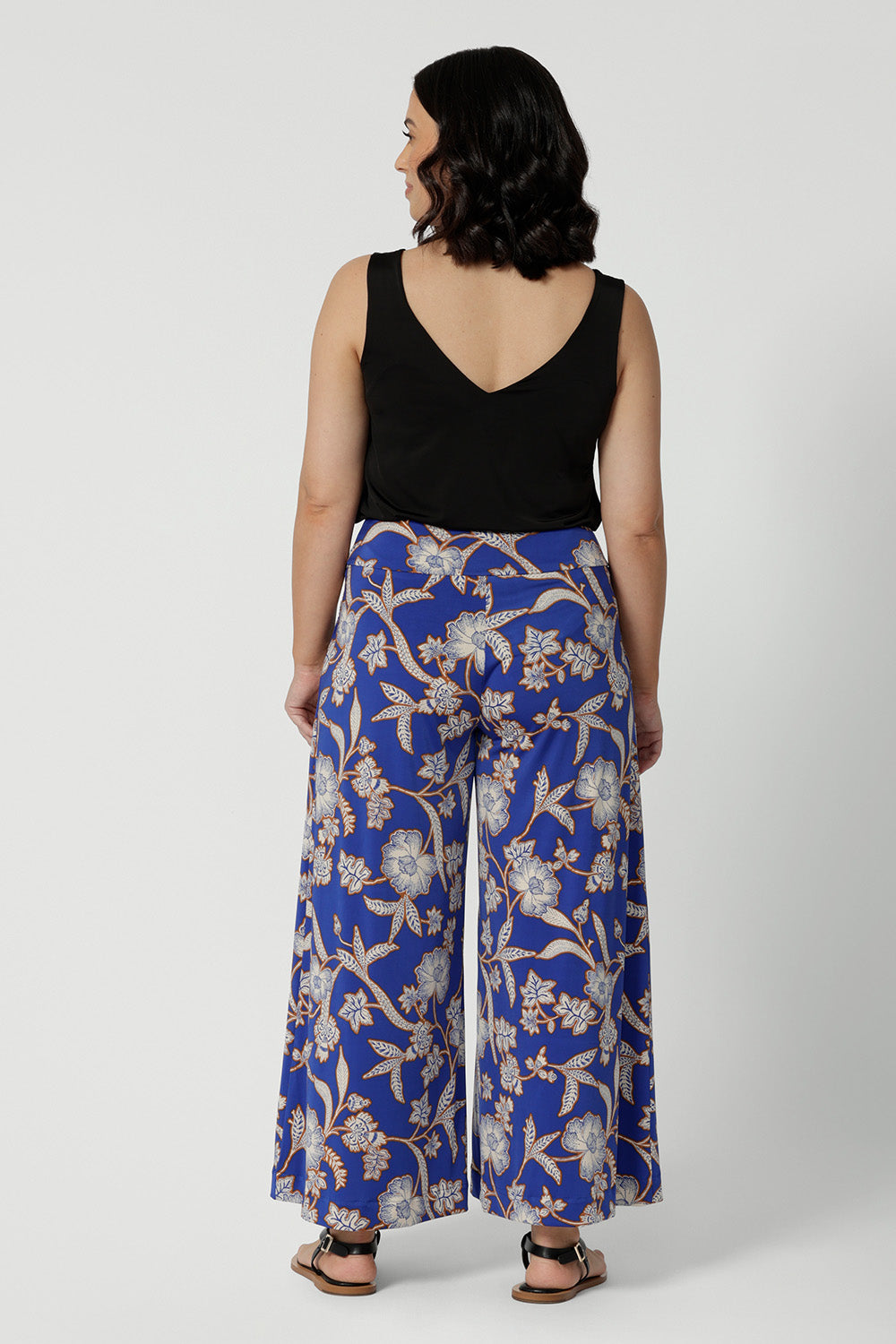 Wide leg pants for summer don't come much better than this! Worn by a size 10, woman, this is a back view of petite friendly wide leg pants in easy care jersey with a blue, caramel and white floral print. Worn with a black cami top, these wide leg culottes are made in Australia by Australian and New Zealand womens clothing brand, Leina and Fleur. Shop wide leg pants in petite to plus sizes.