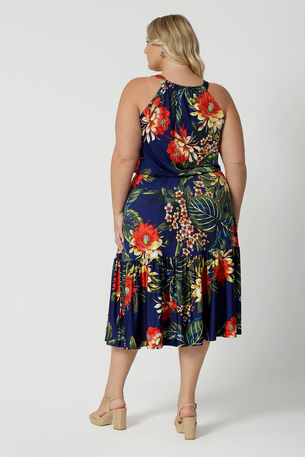 Back view image of plus sized model wears midi floral dress. Dress for summer has a halter neck detail and ruffle hem. Floral fabric use is easy-care and crease-resistant perfect for travel. Leina & Fleur is a womans clothing brand that actively stocks sizes from 8-24. Shop this summer ready dress in petite sizes and plus sizes.