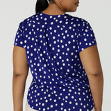 Back view of a size 16 Woman wearing a Cobalt Blue spot top with flutter sleeves, high low hemline and v-neck. Soft slinky jersey. Made in Australia for women size 8 to 24.