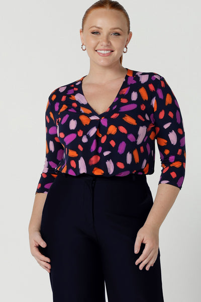 Size 12 woman wears the Jaime top in Palette. A brush stroke inspired abstract print on a navy base with fuchsia, red, orange and pink spots. A v-neck pleat front top great for work to weekend. Comfortable jersey and easy care. Made in Australia for women size 8 - 24. Styled back with navy tailored pants. 