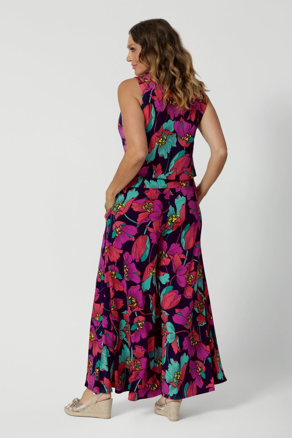 An image of the back of a summer top for curvy women, a size 10 woman over 40  wears a cowl neck jersey top. This sleeveless top has a bold floral print - great for work wear as well as off duty style. Styled with a wide-leg palazzo pant in a matching print. Made in Australia by Australian and New Zealand clothing brand, Leina & Fleur, shop this top in petite to plus sizes. 