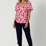 Full body image of 40 year old woman wears red flutter sleeve top with ivory floral details paired with classic black Indi Pant. High quality fabric used to make these garments is dry touch jersey. Made in Australia for woman in Australia & New Zealand. Sizes range from 8 - 24 with plus and petite friendly sizes considered and ready to shop.