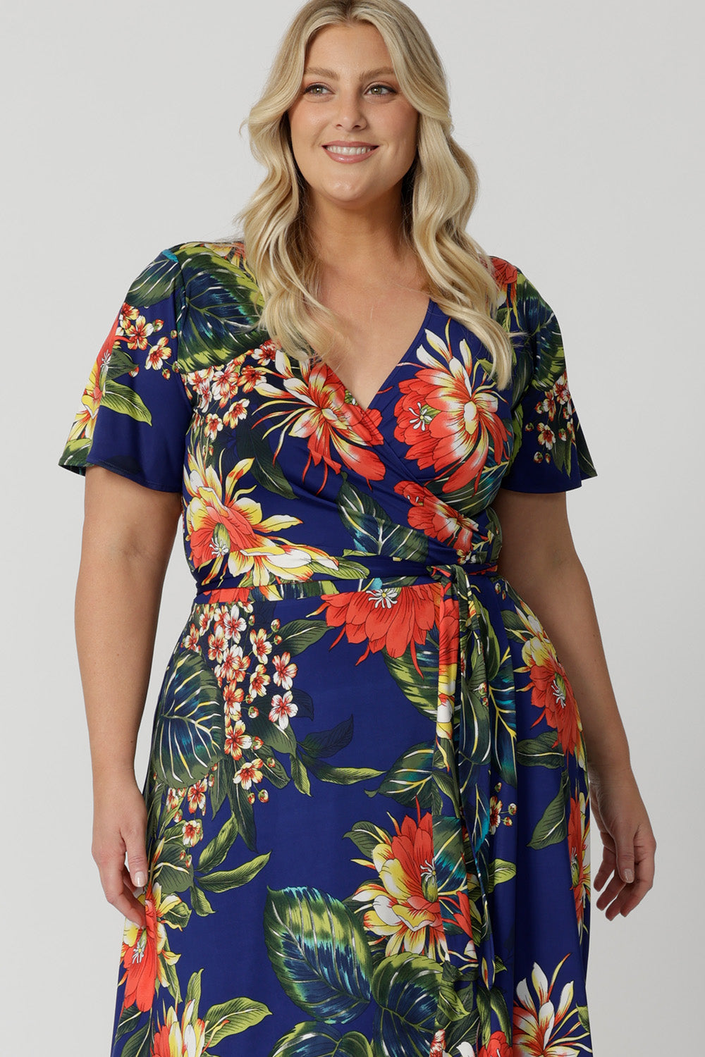 Plus sized model wears maxi dress made with wrap dress detail and flutter sleeve detail. Easy-care and crease-resistant wrap dress is perfect for travel. Leina & Fleur is a woman's clothing brand that have sizes from 8-24. Shop this summer ready dress in petite sizes and plus sizes. Lightweight and packable, fits easily in your luggage for cruise and resort adventures.