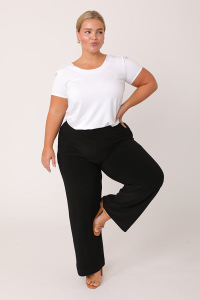A curvy petite height woman wears black trousers in petite length with a white bamboo jersey T-shirt top. Great pants for short women, these black jersey pull-on trousers are available in sizes 8 to 24, petite to plus sizes.