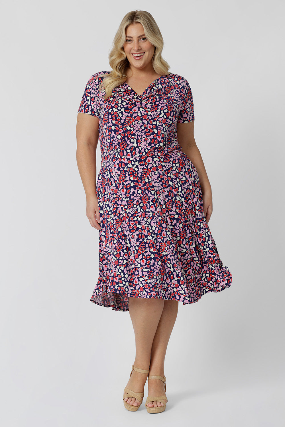 Summer dresses for curve women don't get much beter than this! A size 18, plus size woman wears knee length summer dress with asymmetric hemline and cowl neck. A short sleeve dress in pretty red, pink, white and navy print this is a good jersey dress for travel and cruise wear.  Made in Australia by Australian and New Zealand women's clothes brand, Leina & Fleur, shop their petite to plus size dresses online. 