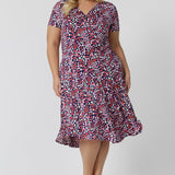 Summer dresses for curve women don't get much beter than this! A size 18, plus size woman wears knee length summer dress with asymmetric hemline and cowl neck. A short sleeve dress in pretty red, pink, white and navy print this is a good jersey dress for travel and cruise wear.  Made in Australia by Australian and New Zealand women's clothes brand, Leina & Fleur, shop their petite to plus size dresses online. 