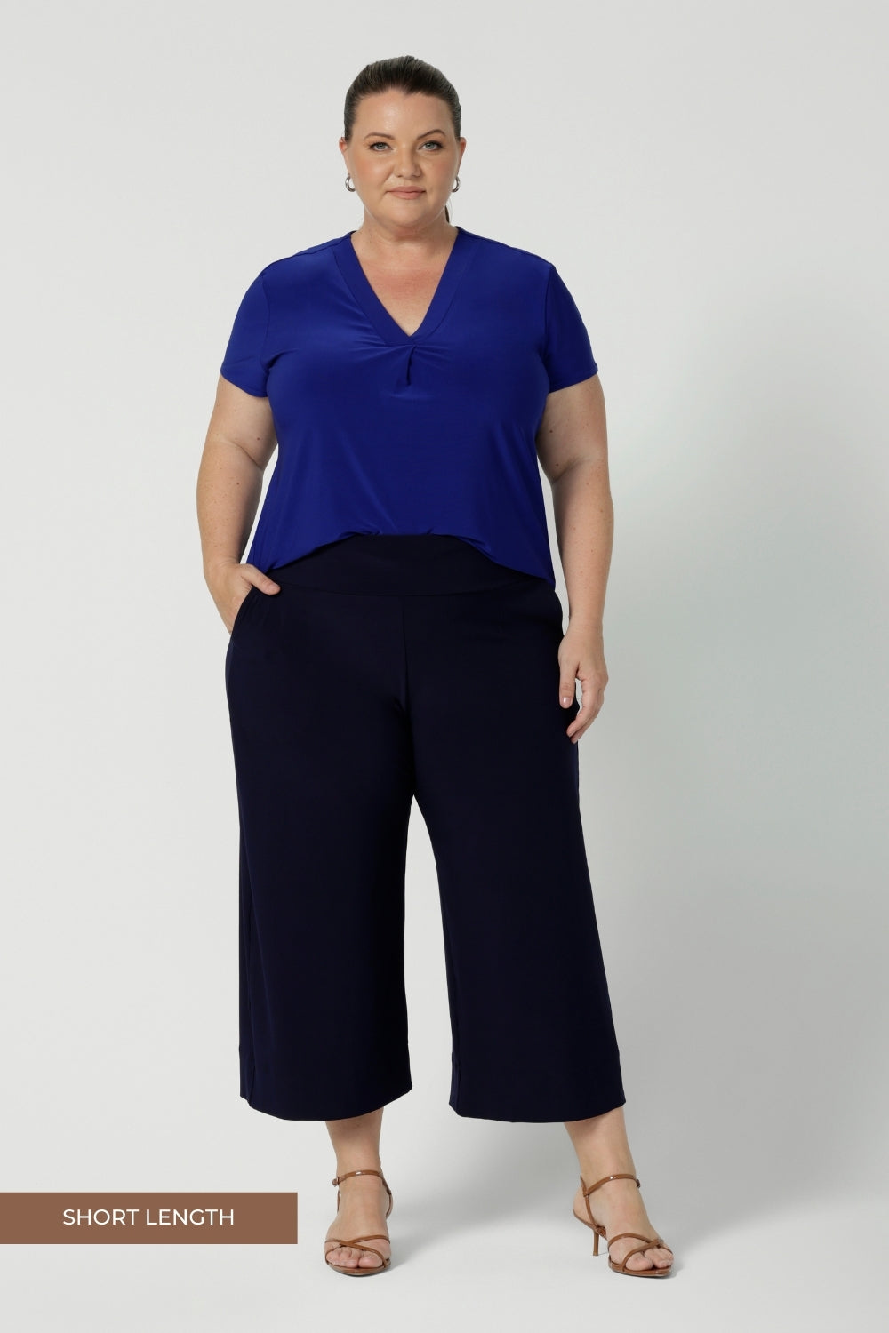 Plus size woman wears wide leg navy pants, paired with cobalt v neck top and brown heels - creating a perfect back to work look. These wide leg pants come in two different lengths for regular & petite sizes.