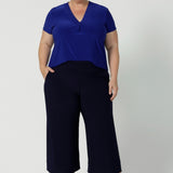 Plus size woman wears wide leg navy pants, paired with cobalt v neck top and brown heels - creating a perfect back to work look. These wide leg pants come in two different lengths for regular & petite sizes.