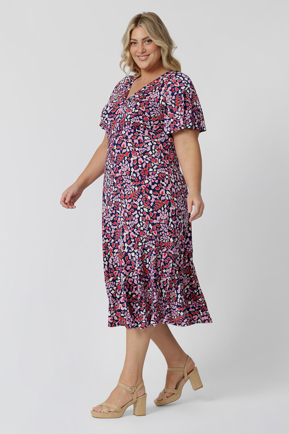 Summer dresses for plus size women doen't get much beter than this! A size 18, curvy woman wears an empire line midi dress with flutter sleeves and twist front bodice. A good dress for wedding guest outfits, the pink, red, white and navy blue print make it a pretty summer dress. Made in Australia by Australian and New Zealand women's clothes brand, Leina & Fleur, shop their petite to plus size dresses online. 