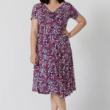 Summer dresses for petite women don't get much beter than this! A size petite size 10 woman wears knee length summer dress with asymmetric hemline and cowl neck. A short sleeve dress in pretty red, pink, white and navy print this is a good jersey dress for travel and cruise wear.  Made in Australia by Australian and New Zealand women's clothes brand, Leina & Fleur, shop their petite to plus size dresses online. 