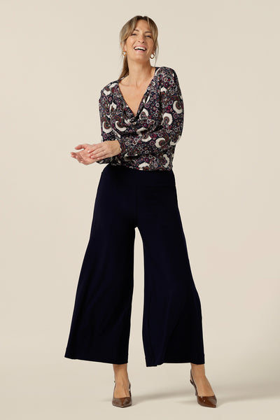A size 10 woman wears wide leg pull-on pants in navy stretch jersey with a paisley print, long sleeve cowl neck top. Comfortable pants for work and casual wear, these cropped trousers are made in Australia by women's clothing brand, Leina & Fleur. 