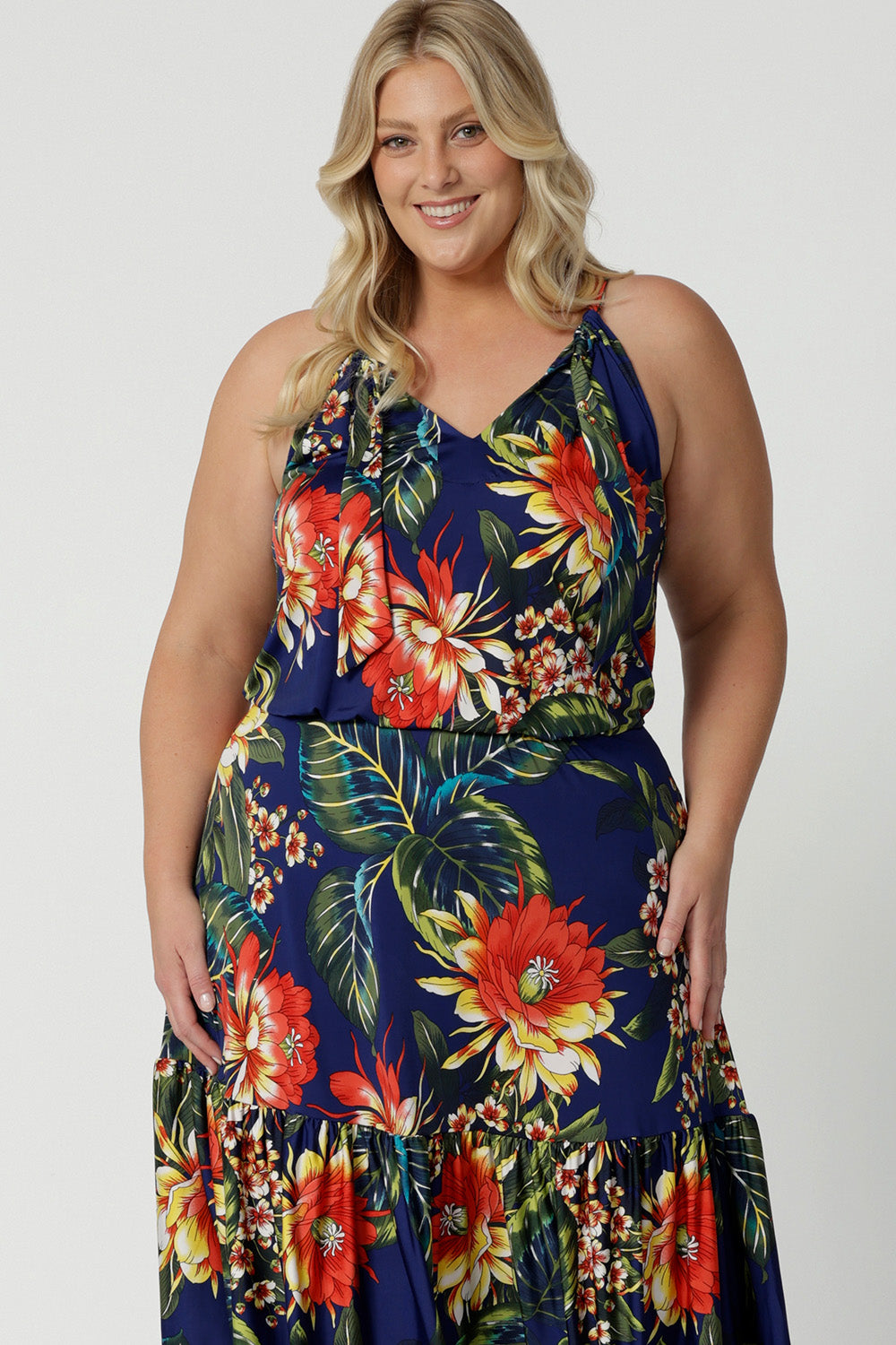 Plus sized woman wears floral midi dress that has halter neck detail and ruffle hem. This easy-care and crease-resistant dress is perfect for travel. Designed in Australia with easy care fabric made of deep blue slinky jersey. Leina & Fleur clothing brand actively stock sizes from 8-24. Shop this summer ready dress in petite sizes and plus sizes.