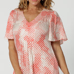 Close up of a dress for over 40s style This silky flutter sleeve dress in viscose fabric has an orange spot print. Made in Australia by women's clothing brand, Leina & Fleur, this lightweight summer dress is breathable. Shop this summer wedding guest and event wear outfit online in sizes 8 to 24.