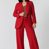 A petite height woman wears the Merit Blazer in Flame, a textured scuba crepe plus size blazer with button front. This red work blazer is worn with red workwear pants and navy work top. Curved hemline and front pockets. This blazer is Made in Australia for petite women in sizes 8 - 24.