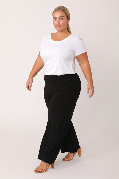 A curvy petite height woman wears black work pants in petite length with a white bamboo jersey T-shirt top. Great pants for petite height women, these black jersey pull-on trousers are available in sizes 8 to 24, petite to plus sizes.