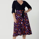 Size 12 woman wears the Nerida dress. Functioning fit and flare wrap dress with a navy bodice and printed skirt. 3/4 Sleeves and functioning pockets. Made in Australia for women. Size 8 - 24. Styled back with a brown sling back heel. 