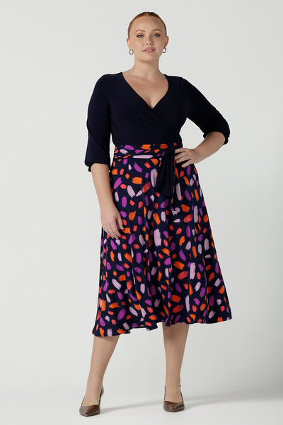 Size 12 woman wears the Nerida dress. Functioning fit and flare wrap dress with a navy bodice and printed skirt. 3/4 Sleeves and functioning pockets. Made in Australia for women. Size 8 - 24. Styled back with a brown sling back heel. 