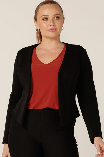 A classic work jacket, the Yuri Jacket in Black is a collarless, open-front, soft tailored jacket. Shown here in a size 12, the jacket is worn with black tailored pants to create a workwear suit look, and a V-neck top in orange. All are made in Australia by Australian and New Zealand women's clothing label, L&F.