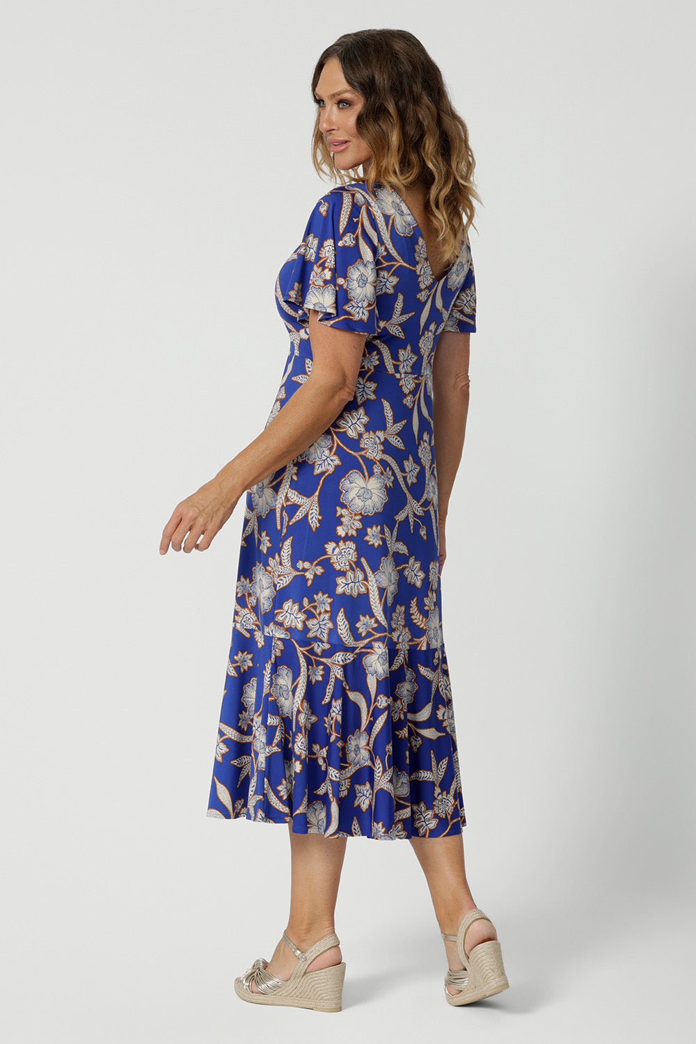 Back view of a good empire line dress for over 40s women With a twist front V neckline, this midi length jersey dress with flutter sleeves also features a ruffle hem. A blue dress with floral print, be holiday ready with this travel and cruise wear dress style. Made in Australia by Australian and New Zealand women's clothes brand, Leina & Fleur, shop their petite to plus sizes dresses online.