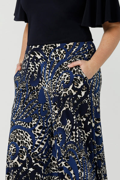 A close up of A curvy size, size 12 woman wears printed wide leg pants with pockets with a navy round neck top. These pull-on, easy care pants are comfortable for your everyday workwear capsule wardrobe. Shop these Australian-made wide leg trousers online in sizes 8 to 24, petite to plus sizes.
