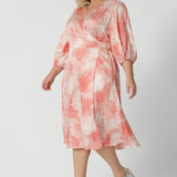 Side view of an event dress for plus size women, this silky wrap dress with orange spot print and 3/4 lantern-shaped sleeves is shown on a size 18, curve woman.. Made in Australia by women's clothing brand, Leina & Fleur, wear this 3/4 sleeve wrap dress for wedding guest outfit and summer event  wear. Shop this summer wedding guest and event wear outfit online in sizes 8 to 24.